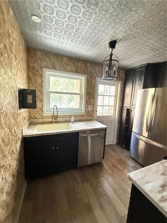 Kitchen featuring wood-finish flooring, recessed sink with a brass-finish faucet, stainless steel dishwasher, stainless steel refrigerator, and dark cabinetry