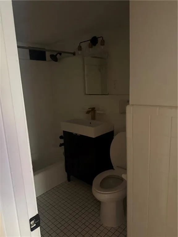 Compact bathroom featuring a white square tile floor, white tub/shower combination, and a dark vanity with a white basin sink