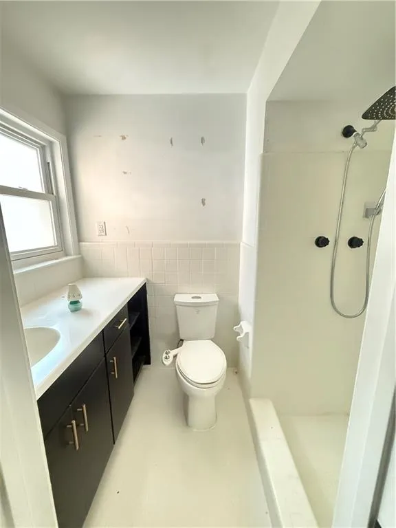 Bathroom featuring a dark wood vanity with a white countertop and integrated sink, a commode, and a shower with a handheld showerhead