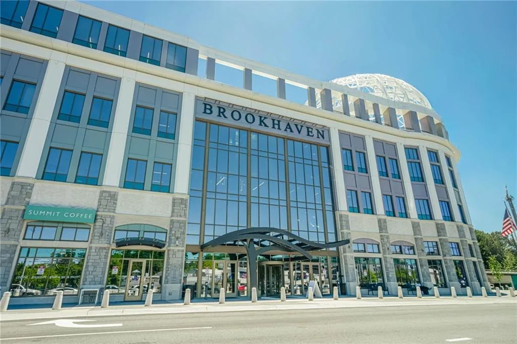 Multi-story commercial building featuring a prominent glass-enclosed entrance, stone facade accents, and a distinctive domed architectural element