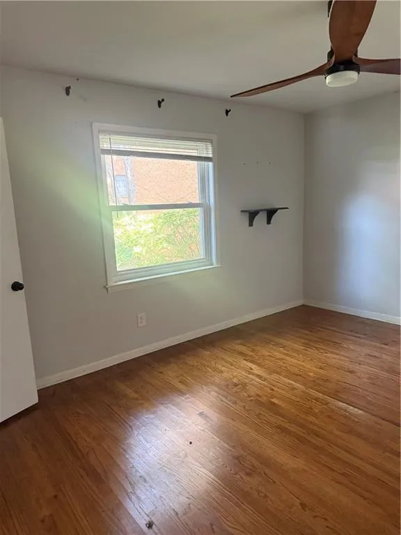 Room featuring wood-finish flooring, a double-hung window with blinds, and a ceiling fan with light fixture