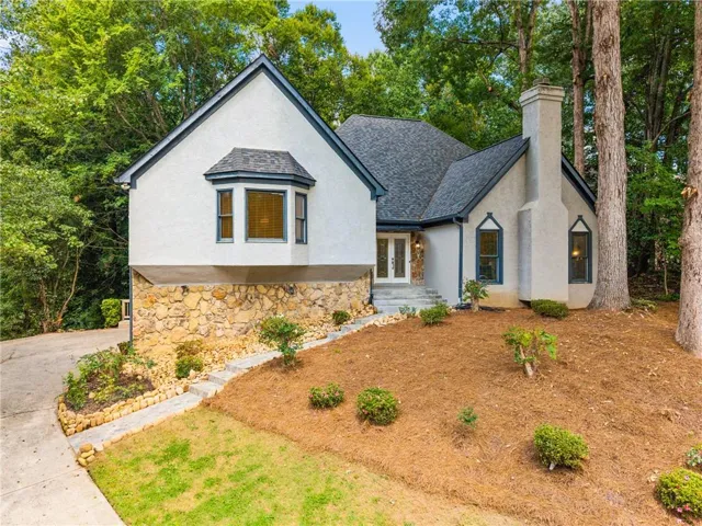 Stucco exterior with stone accenting, dark shingle roofing, prominent bay window, and a grand entry with double doors