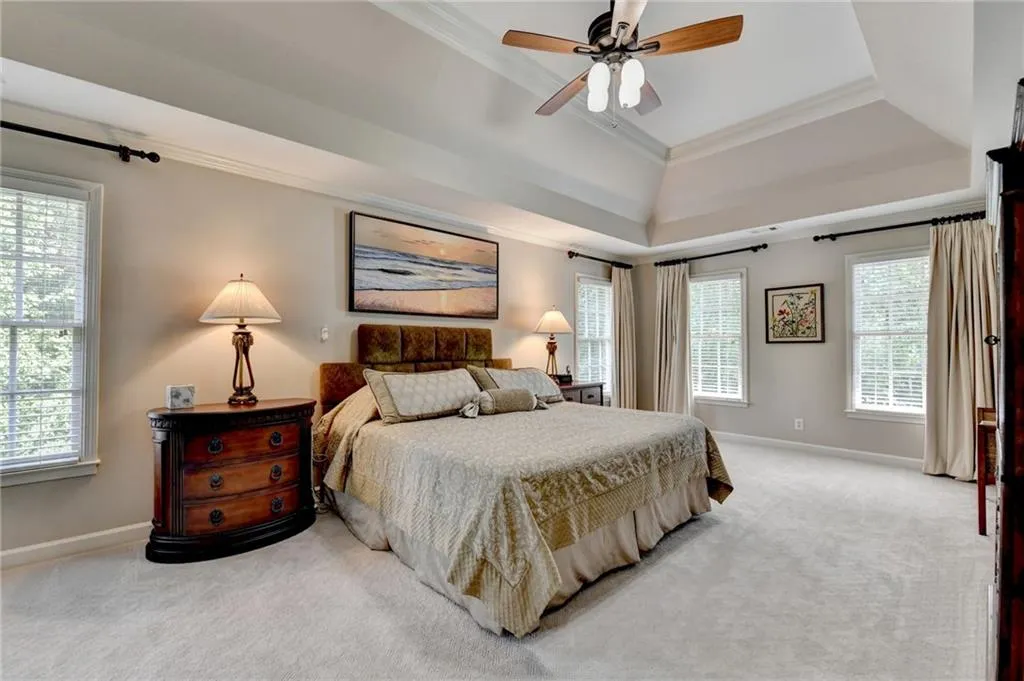 Bedroom with carpet floors, a raised ceiling, ornamental molding, and ceiling fan