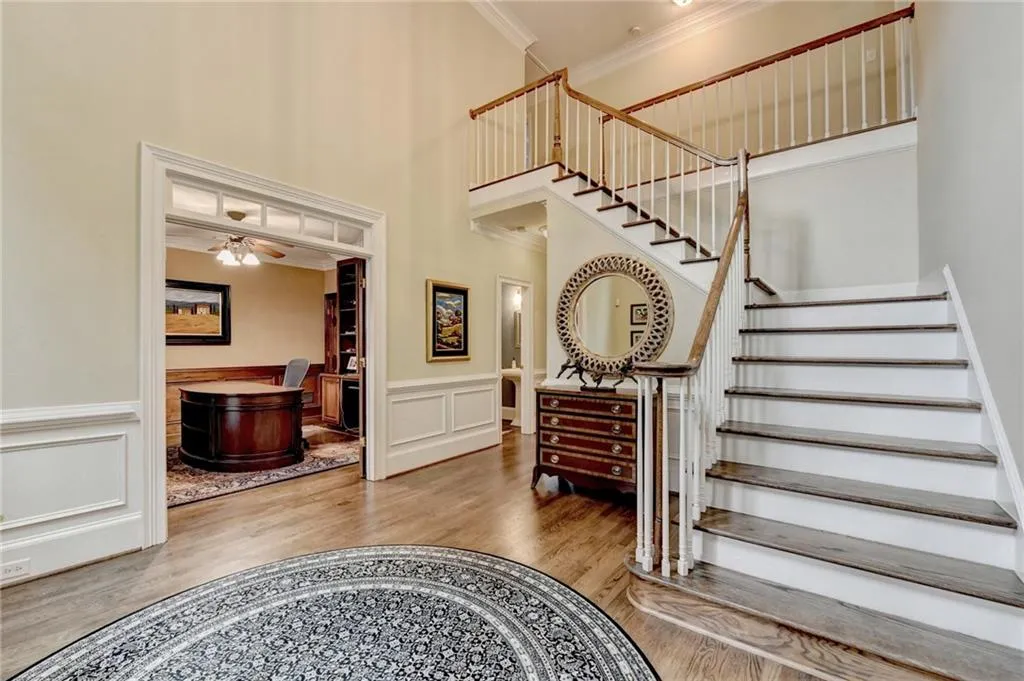 Staircase with crown molding, a towering ceiling, wood finished floors, a ceiling fan, and a wainscoted wall