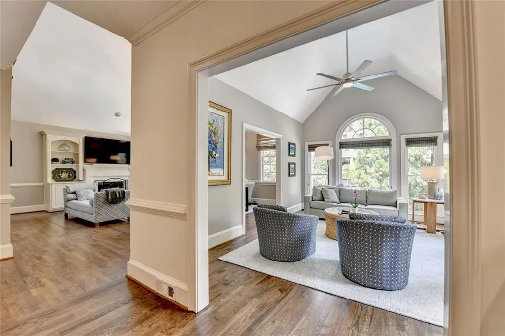 Living area featuring wood finished floors, a fireplace, a ceiling fan, high vaulted ceiling, and crown molding