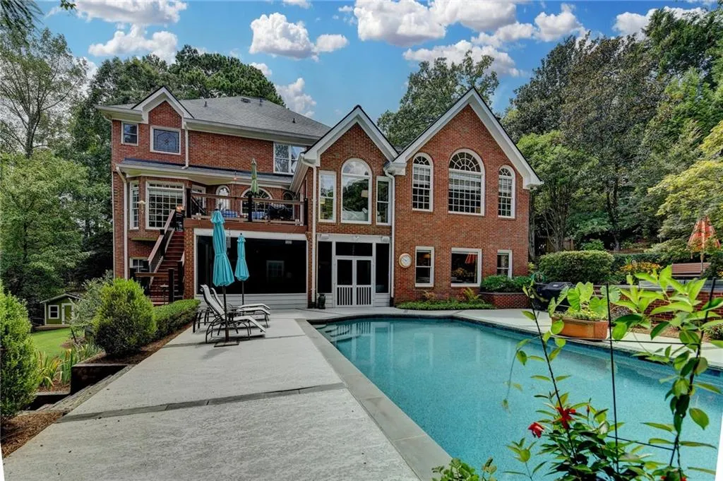 Rear view of property featuring stairs, a patio area, a sunroom, brick siding, and an outdoor pool