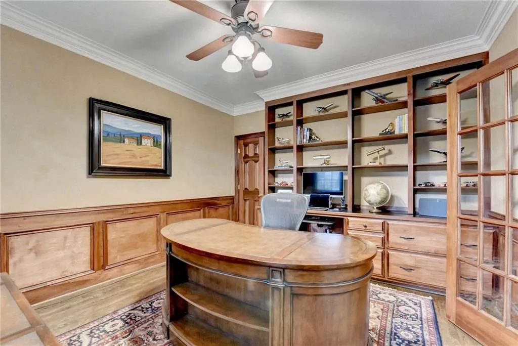 Office space with ornamental molding, light wood finished floors, wainscoting, and ceiling fan