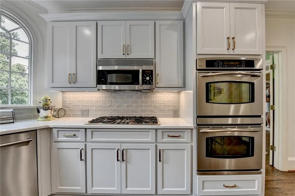 Kitchen with appliances with stainless steel finishes, backsplash, white cabinetry, crown molding, and light stone countertops
