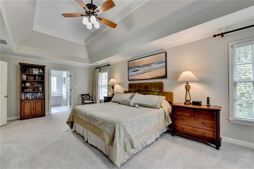Bedroom featuring ornamental molding, light carpet, connected bathroom, multiple windows, and a raised ceiling