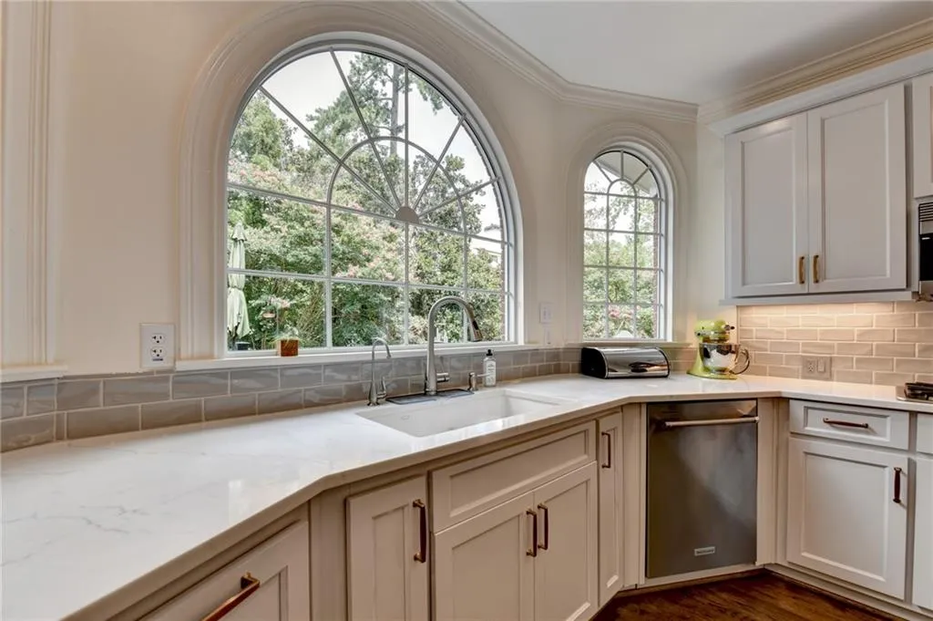Kitchen featuring light stone counters, crown molding, stainless steel dishwasher, decorative backsplash, and dark wood finished floors
