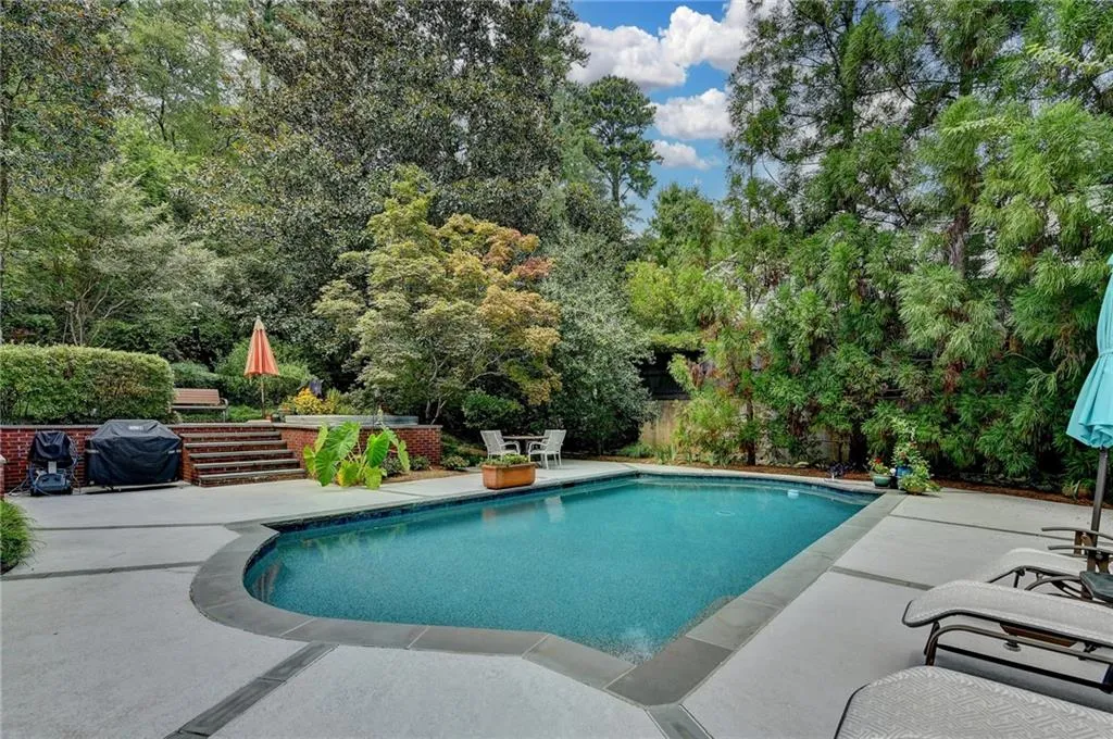 Outdoor pool featuring a patio, grilling area, and view of wooded area