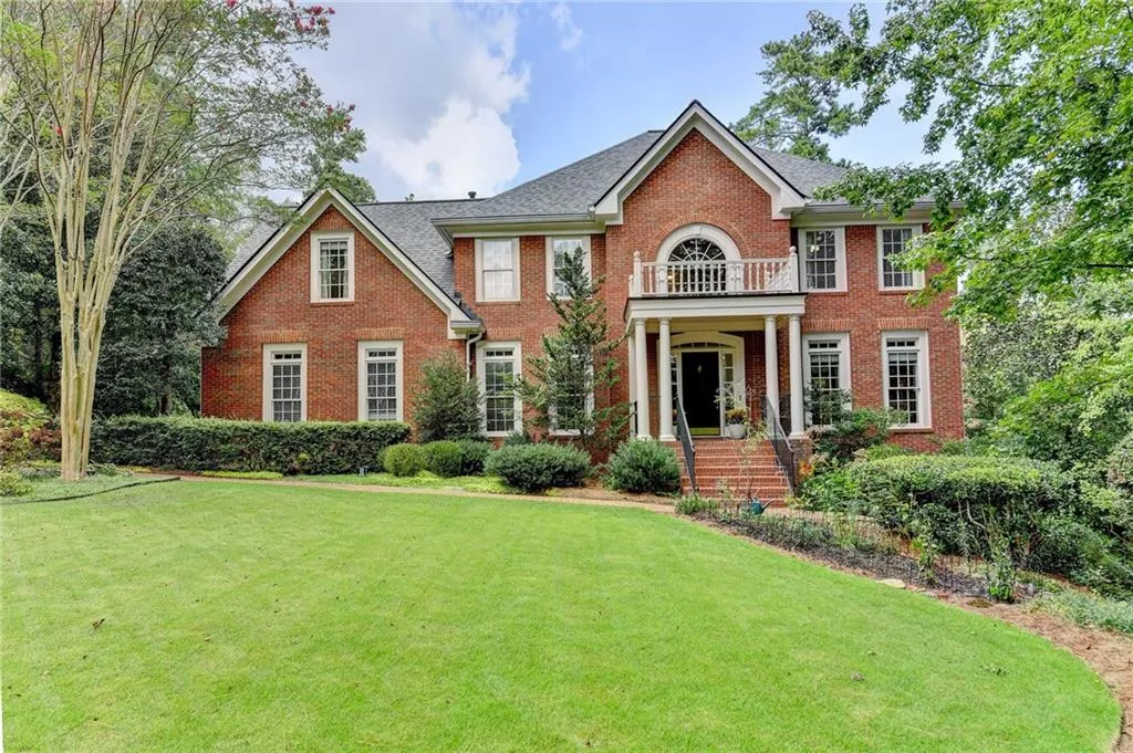 Colonial-style house with brick siding, a front lawn, and a balcony