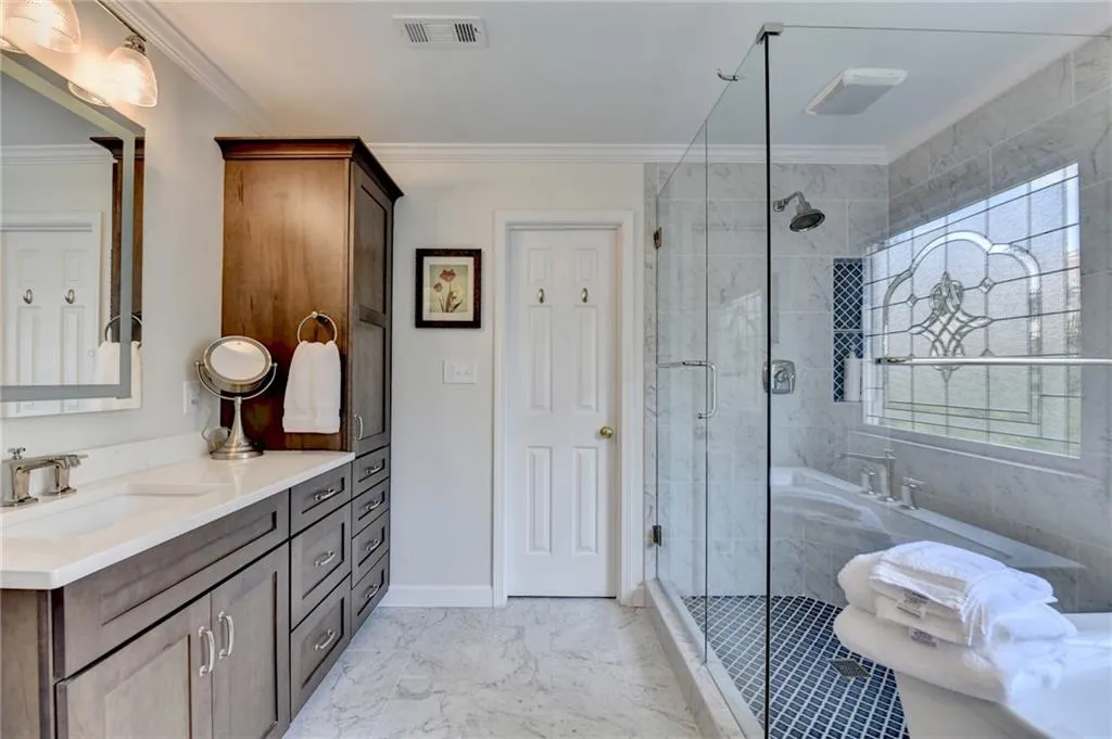 Bathroom featuring a shower stall, vanity, ornamental molding, and light marble finish floors