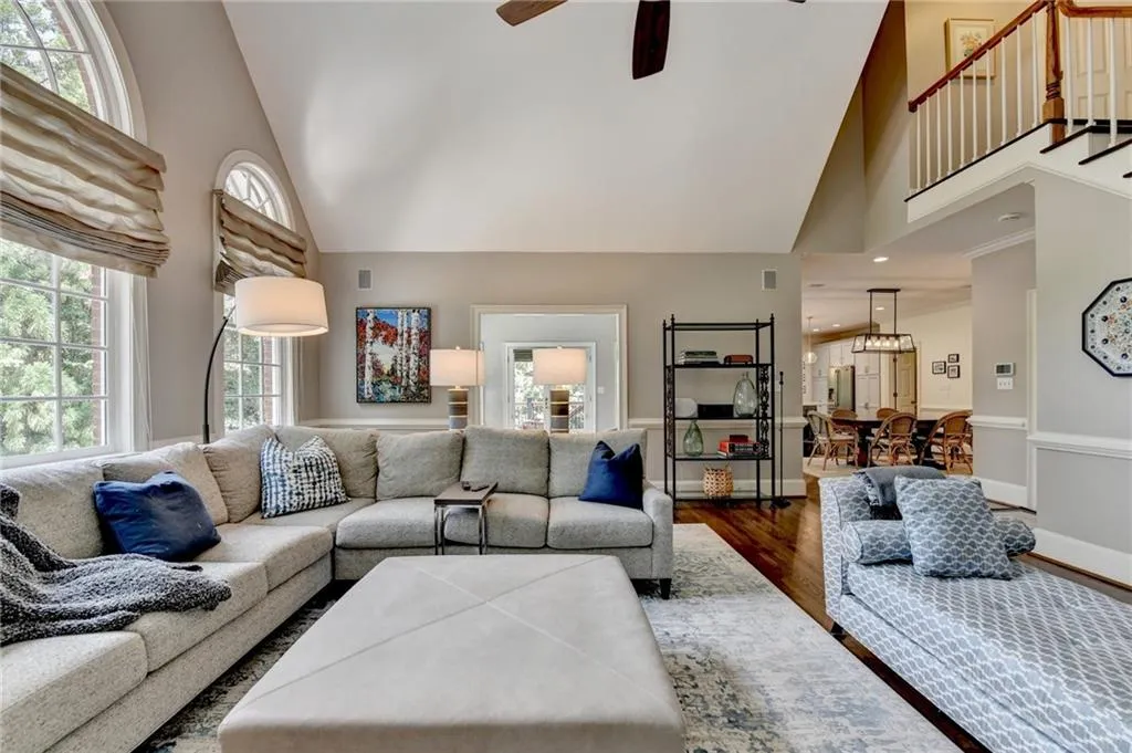 Living area featuring high vaulted ceiling, dark wood-style flooring, ceiling fan, and stairway