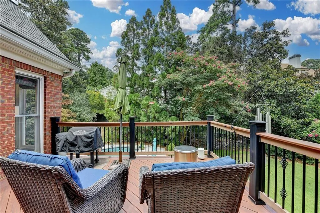 Wooden deck featuring view of scattered trees and a grill