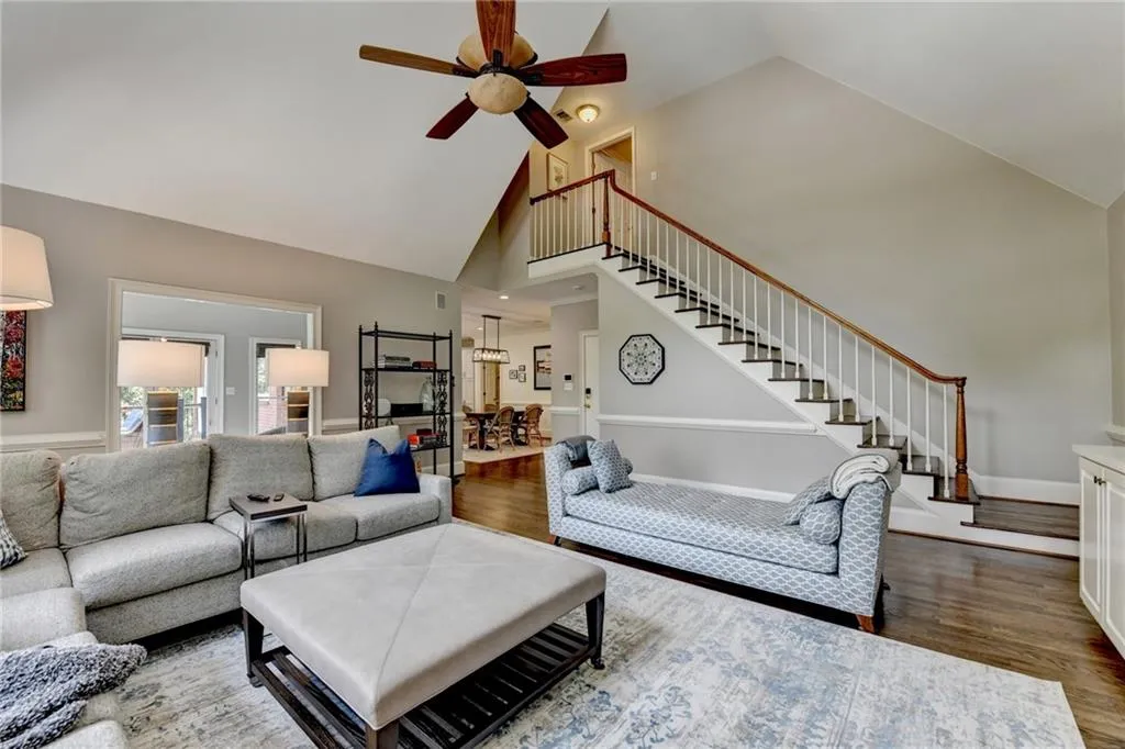 Living room with high vaulted ceiling, dark wood finished floors, ceiling fan, and stairway