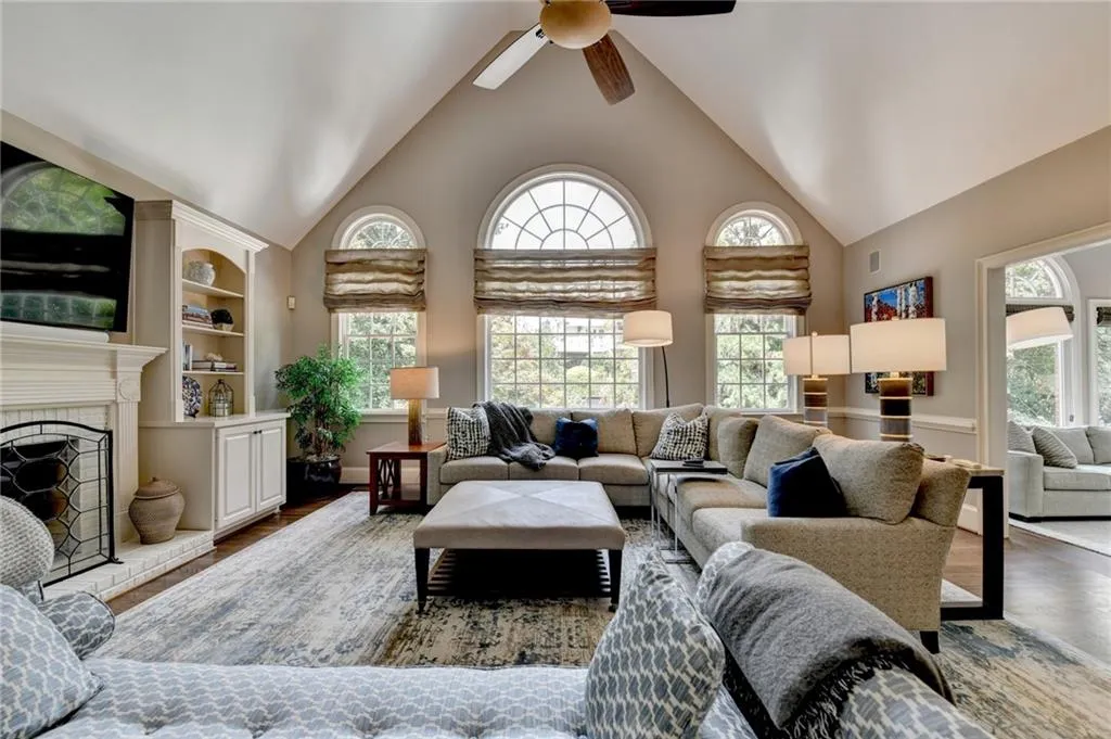 Living room with high vaulted ceiling, a brick fireplace, wood finished floors, and a ceiling fan