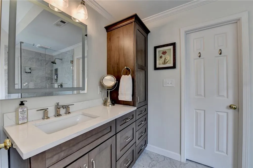 Full bath featuring a walk in shower, crown molding, vanity, and light marble finish floors