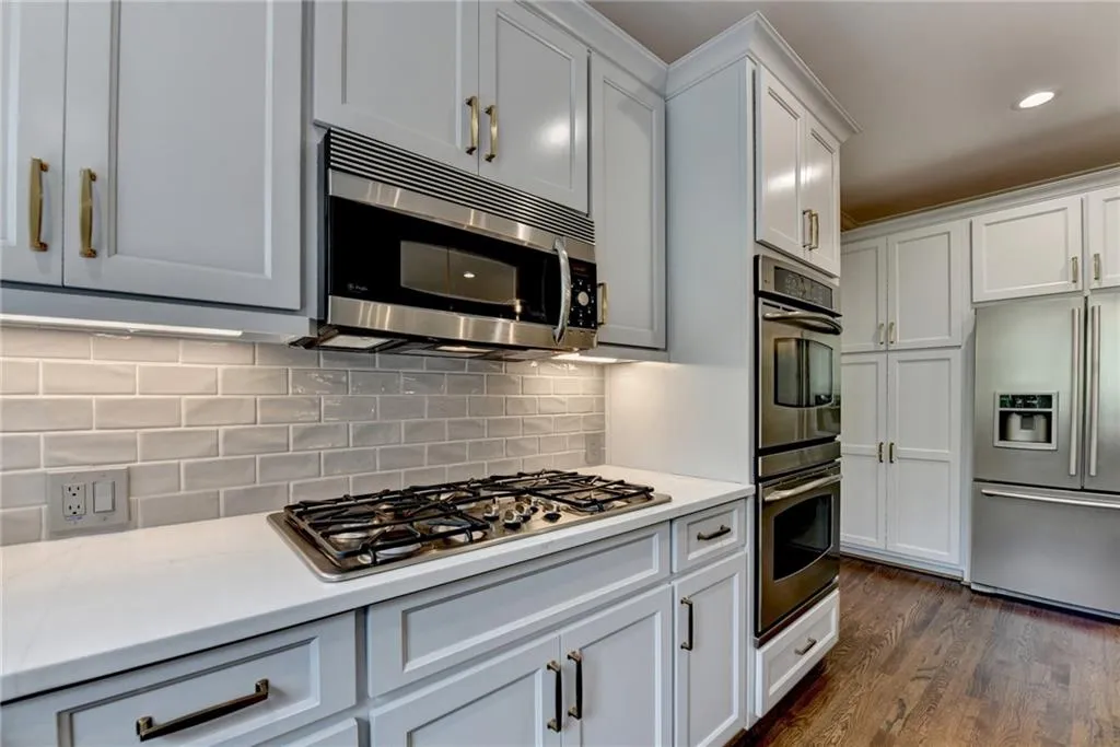 Kitchen with stainless steel appliances, decorative backsplash, dark wood finished floors, recessed lighting, and light stone counters