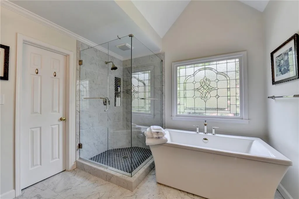 Full bath with a shower stall, a soaking tub, marble look tiles, plenty of natural light, and lofted ceiling