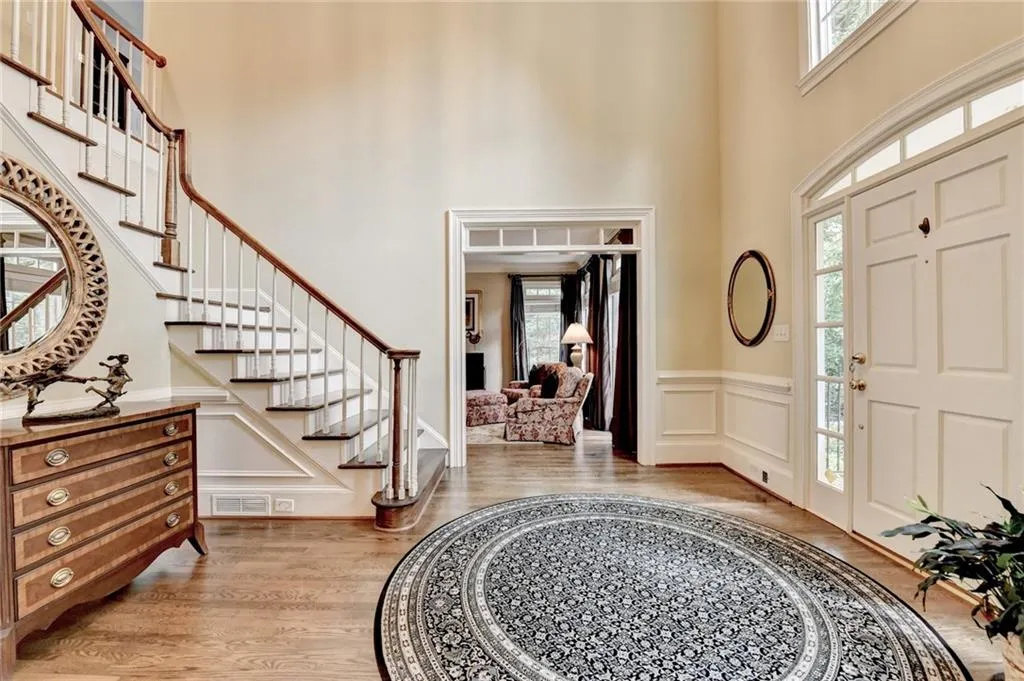 Foyer featuring a decorative wall, light wood-style flooring, wainscoting, a towering ceiling, and stairway
