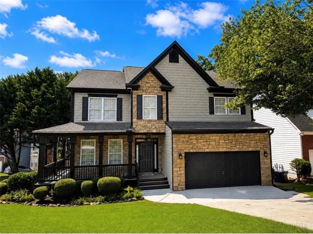 Two-story residence featuring stone and siding exterior, an attached garage, covered front porch, and manicured landscaping