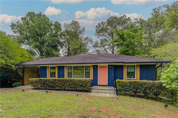Exterior featuring a blue brick facade, contrasting peach entry door, yellow window shutters, and a covered carport with slatted wood detailing