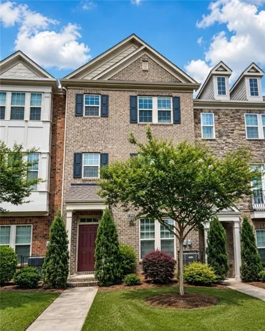 Brick façade townhouse featuring dark-toned window shutters, a prominent dormer window, and mature landscaping