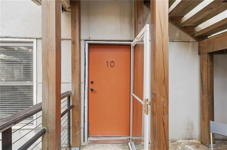 Entryway featuring a bright orange door, a white storm door, and a light wood-finish railing with metal balusters