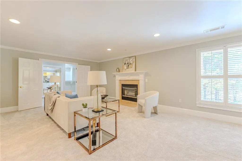 Luxurious primary retreat with fireplace and lounge area featuring molding, light colored carpet and recessed lighting