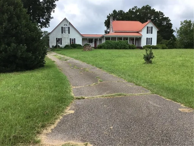 White exterior with a red metal roof, covered porch, and green landscaping