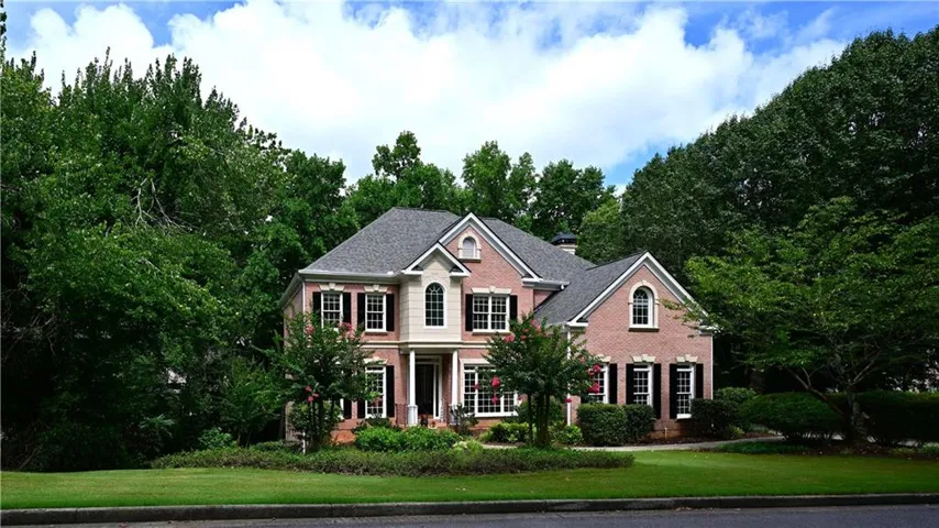 Traditional brick exterior featuring a multi-gabled roofline, prominent bay window, black louvered shutters, and a covered porch entry