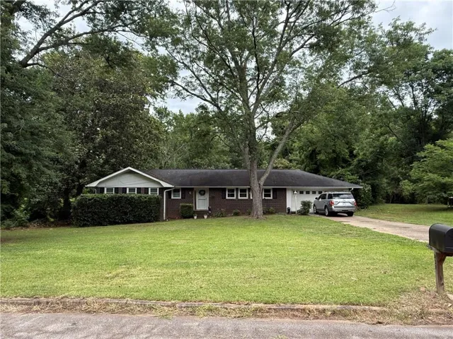Brick exterior residence featuring a front lawn with mature trees, a driveway, and an attached carport