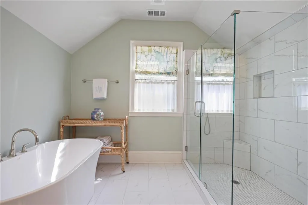 Bathroom featuring a stall shower, a freestanding tub, light marble finish floors, and lofted ceiling