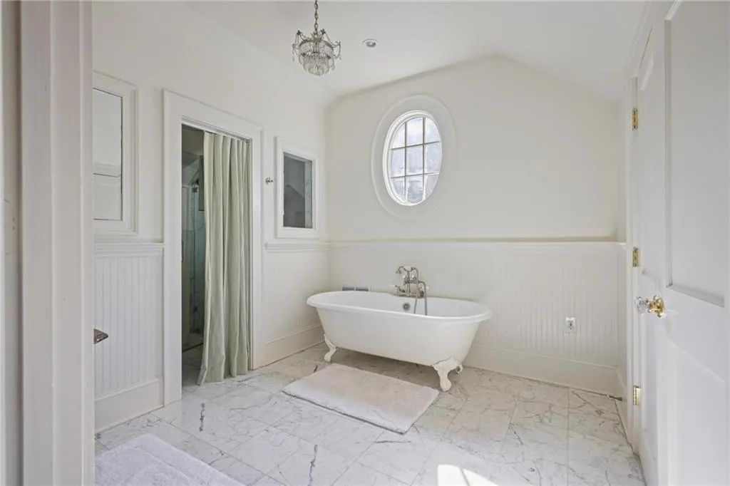 Full bathroom with a wainscoted wall, a soaking tub, light marble finish flooring, lofted ceiling, and a chandelier