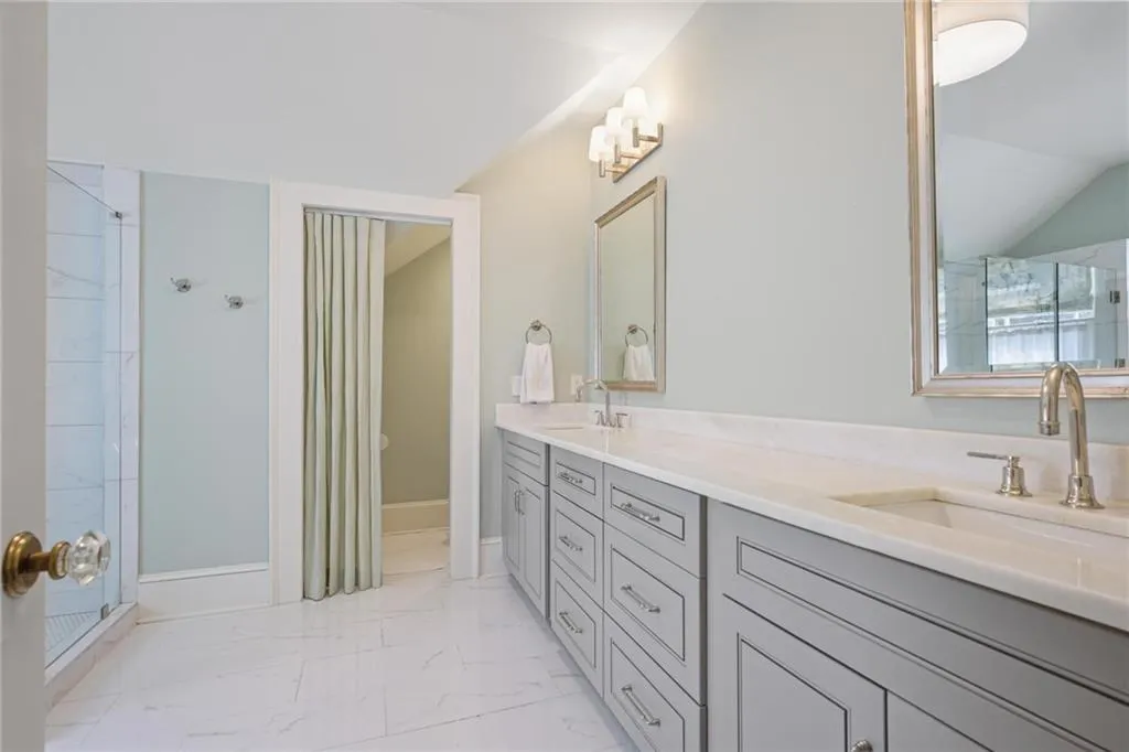 Full bathroom featuring double vanity, lofted ceiling, and light marble finish flooring