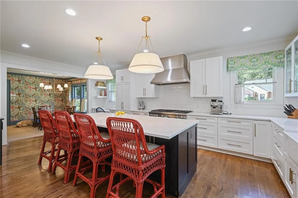 Kitchen featuring pendant lighting, white cabinets, crown molding, wall chimney exhaust hood, and light stone countertops