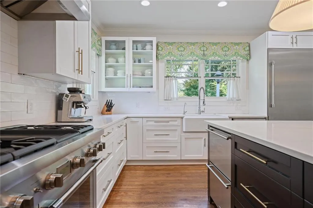 Kitchen with white cabinets, high end appliances, wall chimney exhaust hood, crown molding, and glass insert cabinets