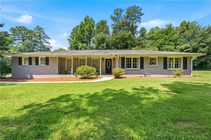 Ranch-style residence featuring a brick exterior with white trim, dark shutters, a covered front entry, and a front lawn with mature landscaping