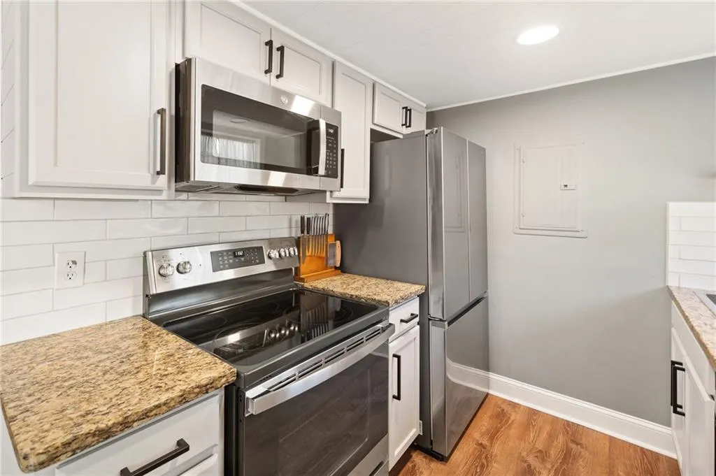 Kitchen featuring backsplash, light stone countertops, appliances with stainless steel finishes, light hardwood / wood-style floors, and white cabinetry