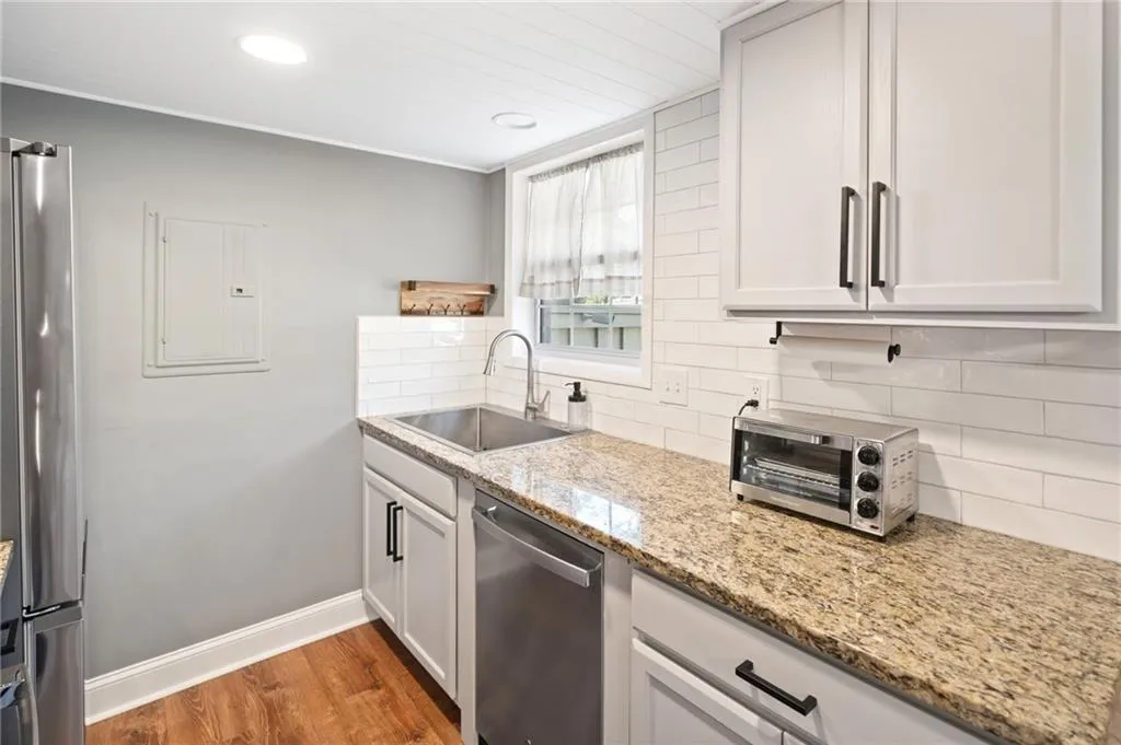 Kitchen with white cabinetry, sink, light stone counters, dark hardwood / wood-style flooring, and appliances with stainless steel finishes