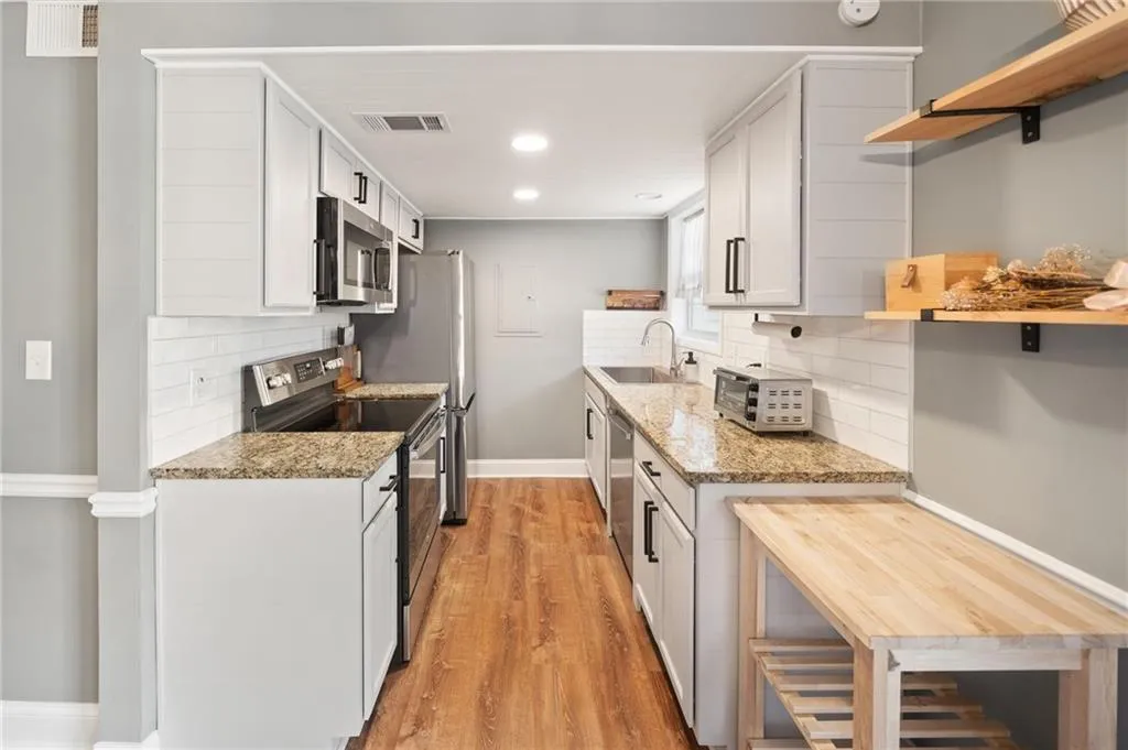 Kitchen with light stone countertops, stainless steel appliances, sink, light hardwood / wood-style flooring, and white cabinets