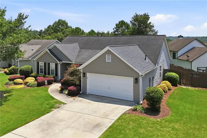 Charming single-story residence featuring a two-car attached garage with white panel doors, gray composite roofing, and neutral exterior siding