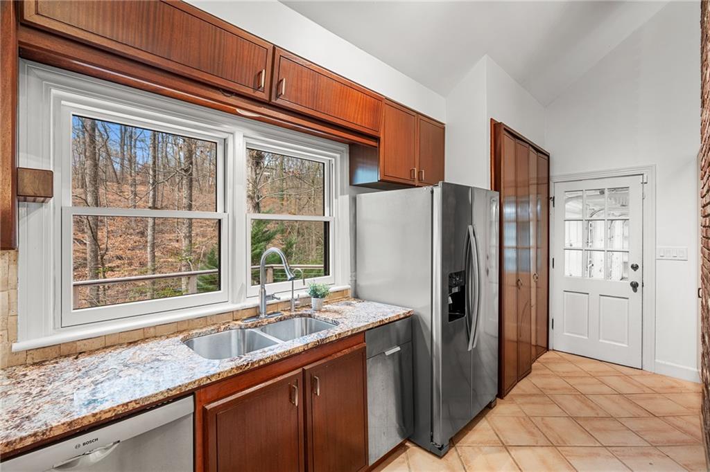 Kitchen with light tile flooring, light stone countertops, appliances with stainless steel finishes, lofted ceiling, and sink