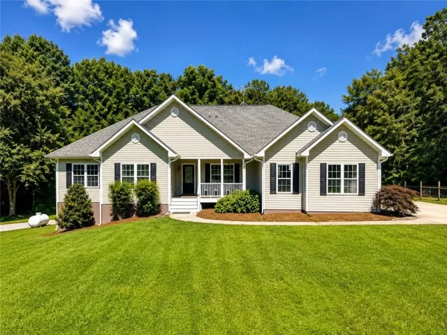 Ranch-style residence featuring light-colored siding, a covered front porch with white columns, and black louvered shutters