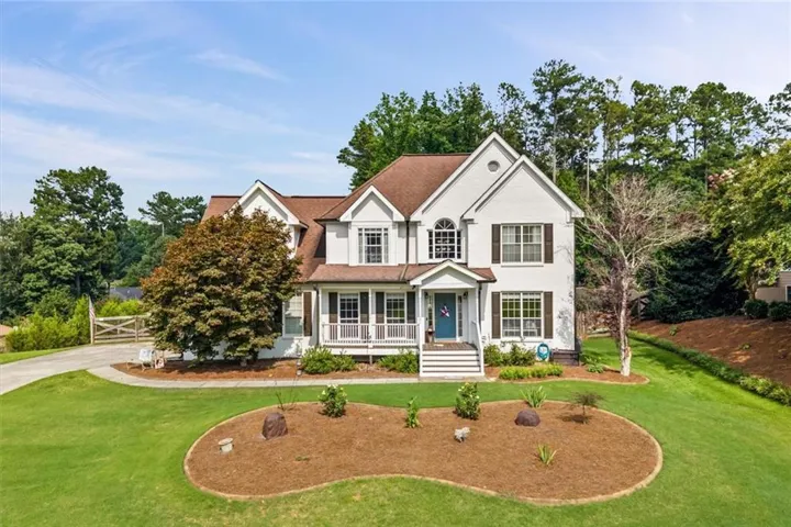 Traditional white two-story residence featuring a brown shingle roof, dark shutters, and a covered front porch with white railings