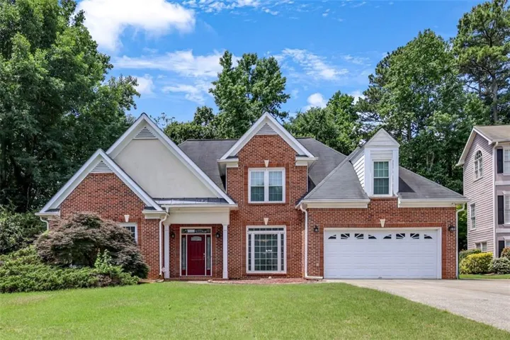 Traditional brick-front residence featuring a red entry door, white trim, and a two-car garage with decorative windows
