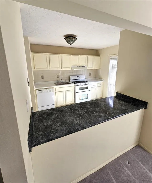 Kitchen with white cabinetry, sink, white appliances