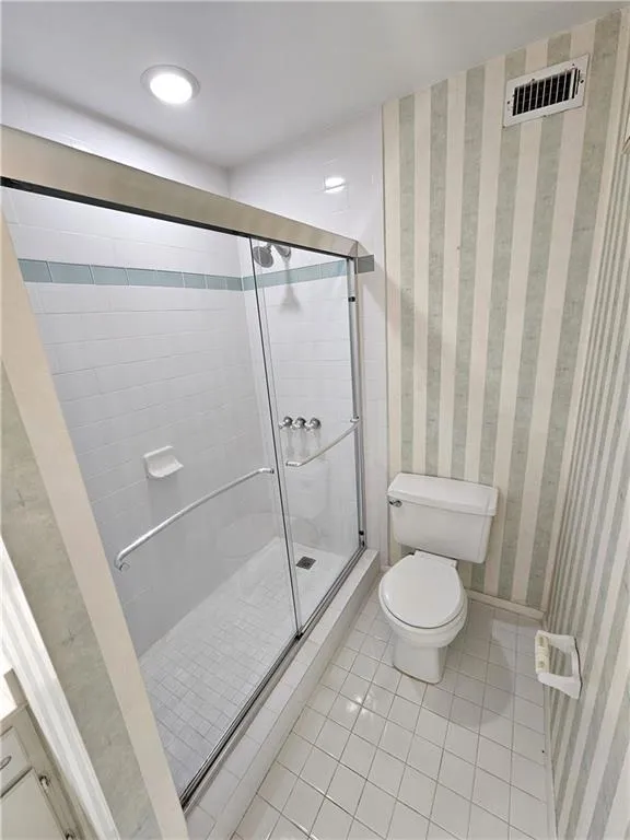 Bathroom with tile floors, a shower with door, and toilet
