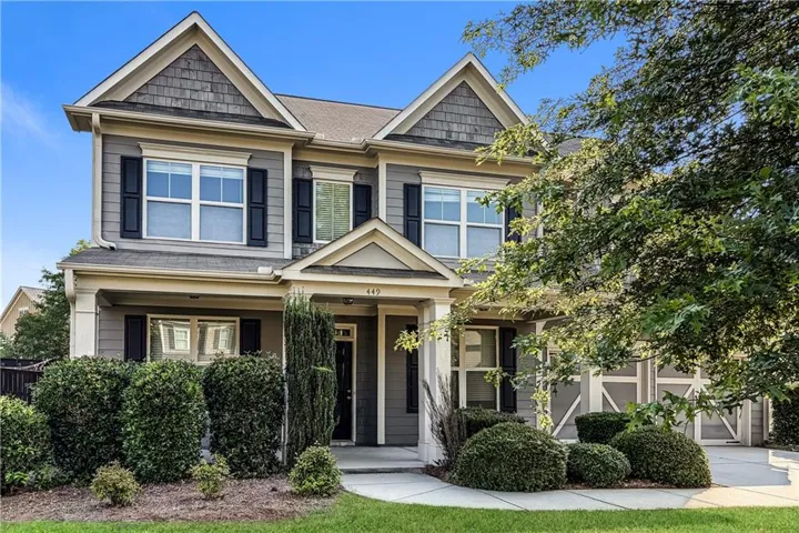 Two-story residence featuring a gabled roofline, shake siding accents, shuttered windows, a covered front porch, and an attached two-car garage with decorative doors